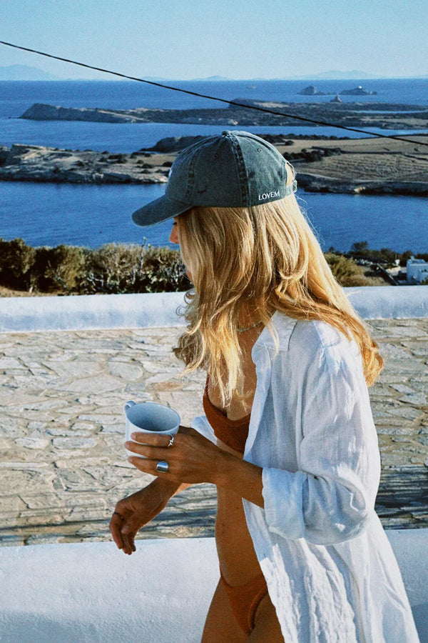Woman in a bikini and cap holding a drink, with a scenic ocean view in the background